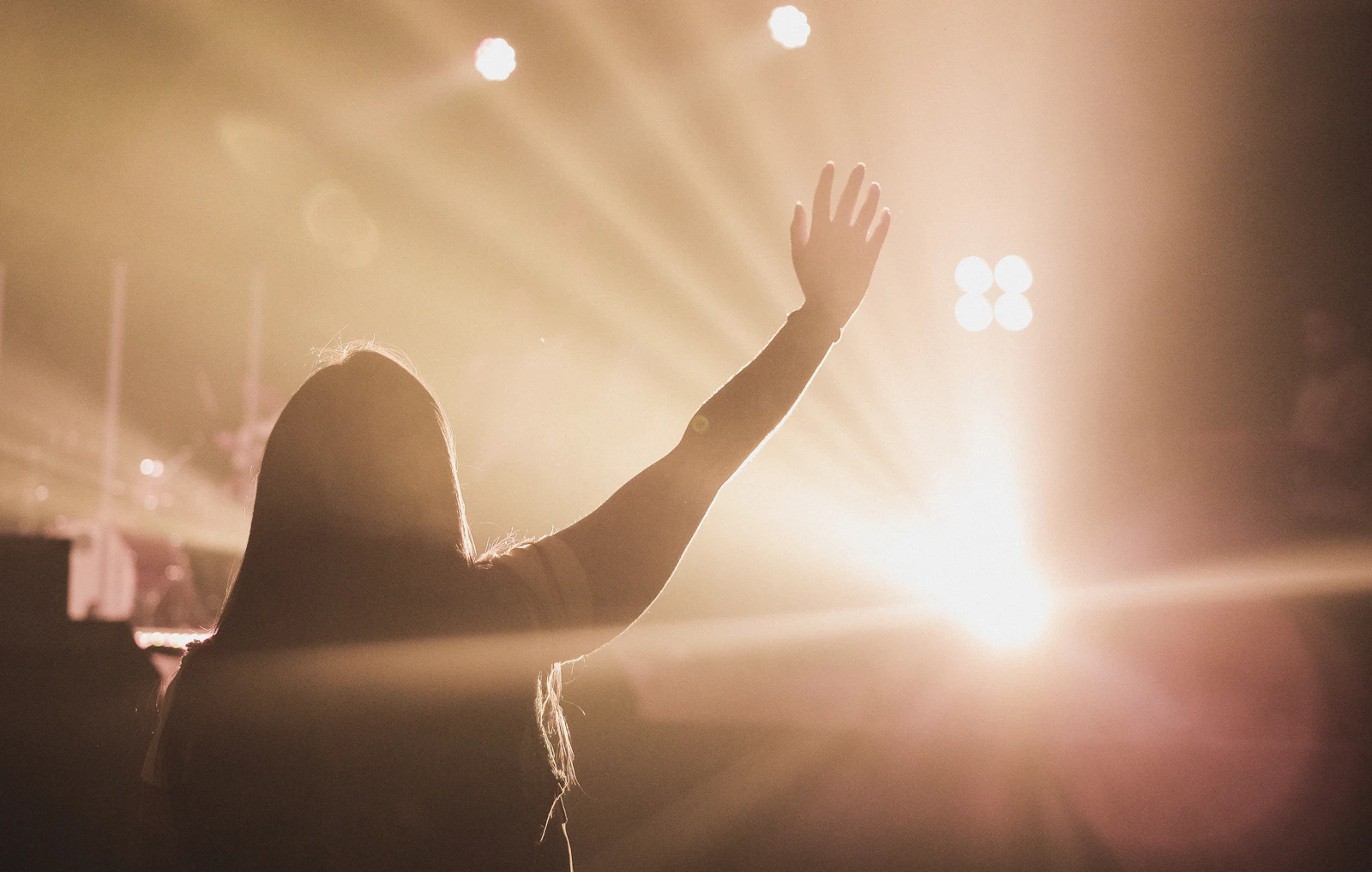 Worshiper raising a hand toward warm stage lights